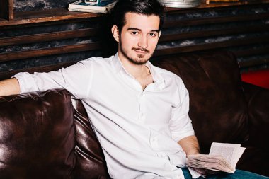 Yakışıklı işadamı bir kitap okuma, gözlük tutan ve evde kanepede otururken gülümseyen