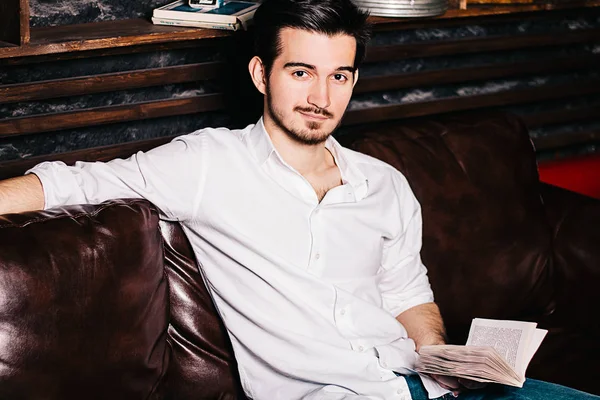 Yakışıklı işadamı bir kitap okuma, gözlük tutan ve evde kanepede otururken gülümseyen