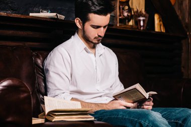 Yakışıklı işadamı bir kitap okuma, gözlük tutan ve evde kanepede otururken gülümseyen