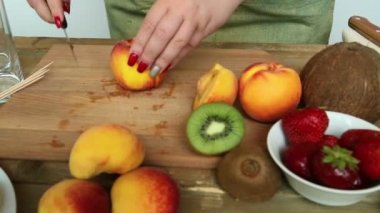 Kütük kesme tahtası muz üzerinde meyve kokteyli için çilek, şeftali. Bir kadın bir şeftali bıçak koşuyor. Sağdan sola doğru kamera hareketli