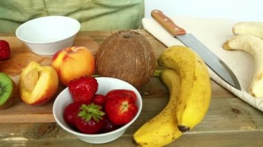 Kütük kesme tahtası muz üzerinde meyve kokteyli için çilek, şeftali. Bir kadın bir kase çilek koyar.