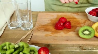 Kütük kesme tahtası muz üzerinde meyve kokteyli için çilek, şeftali. Bir kadın bir plaka çilek alır ve bir kesme tahtası üzerinde koyar.