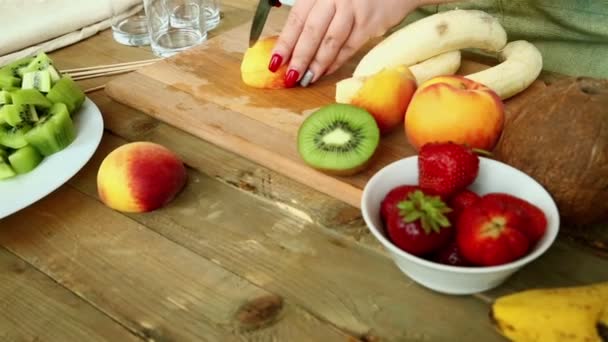 Billetera para cóctel de frutas en una tabla de cortar plátanos, fresas, melocotón. Le dispararon a Dolly. Regimiento de mujeres con cuchillo de melocotón . — Vídeo de stock