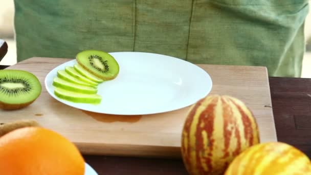 Een Vrouw Zet Stukjes Kiwi Die Een Snijplank Een Bord — Stockvideo