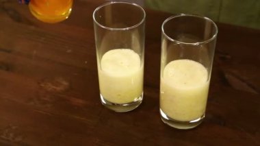 Bir kadın portakal suyu smoothies için ezilmiş muz ile gözlük içine dökülen. Yakın çekim.