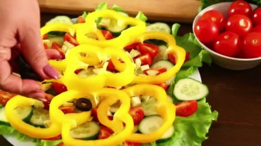 Bir kadın bir tabakta sebze salatası ile siyah zeytin parçaları koyar. Yakın çekim.