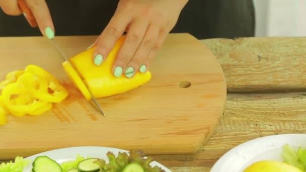 Una mujer sostiene un cuchillo en su mano y corta pimienta amarilla en rebanadas para ensalada . — Vídeo de stock