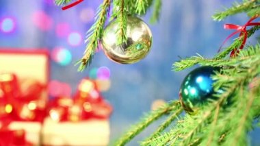 Topları ile süslenmiş Noel ağacı bulanık ve odak hediyeler kırmızı yay ile döner. Mavi bir arka plan üzerinde yan herlands ile. Sağdan sola dolly için kamera hamle.