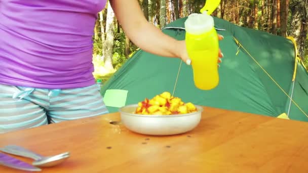 As mãos femininas cortam uma maçã com uma faca em partes da salada de fruto em um piquenique . — Vídeo de Stock