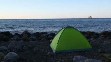 Batan güneşin zemin karşı taşlı deniz plaj üzerinde turist çadır. Statik kamera.