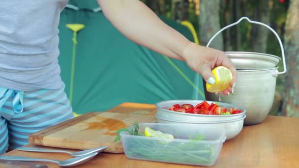 Молодая женщина выжимает лимонный сок в миску с салатом на пикнике . — стоковое видео