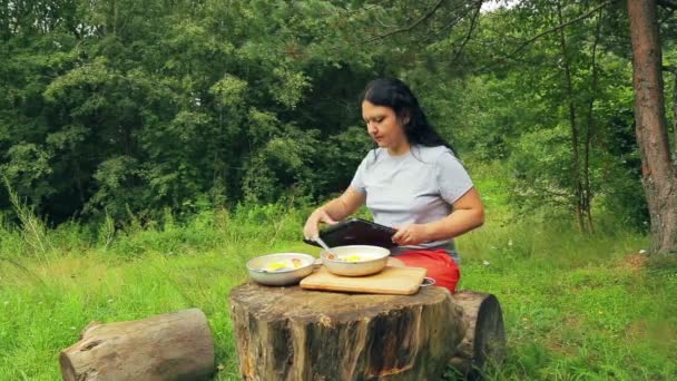 Una mujer que trabaja con un ordenador portátil en el borde del bosque se acuesta y comienza a comer una ensalada de frutas . — Vídeo de stock