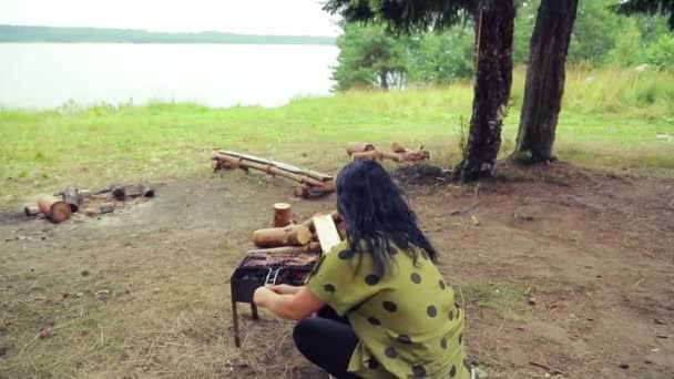 Жінка сидить на барбекю і крутиться над грилем з рибою . — стокове відео