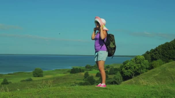 Une femme dans un chapeau de paille avec un sac à dos monte la montagne le long du chemin. tir sur le côté . — Video