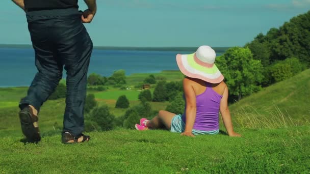 Un uomo e una donna sono seduti sul bordo della montagna e ammirano la vista del lago. tiro da dietro . — Video Stock