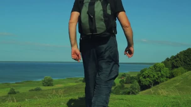 Un hombre con una mochila camina hasta el borde de la montaña con vistas al lago. disparando por la espalda . — Vídeos de Stock