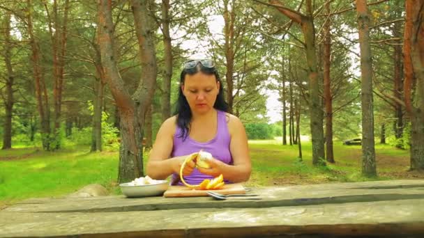 Mulher em um parque em uma mesa de madeira derrama uma salada de frutas de suco de limão para um piquenique . — Vídeo de Stock