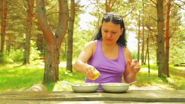 La donna in un parco su un tavolo di legno versa un'insalata di frutta di succo di limone per un picnic . — Video Stock