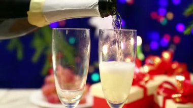 Şişeden shompanskoe iki bardak masanın üzerine yeni yıl arka ışıklarla hediyeler ile bulanık herlings bokeh içinde dökülür.