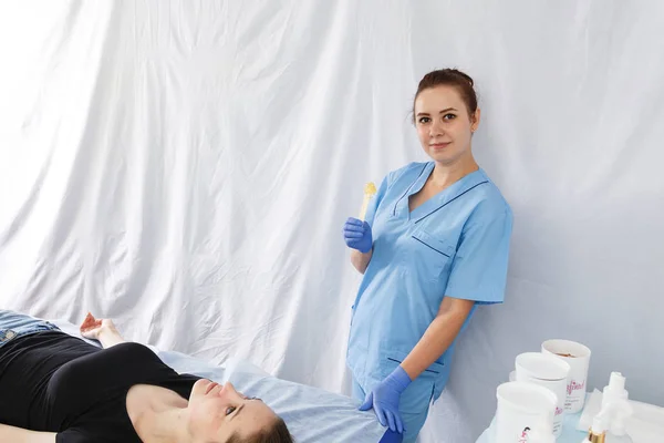 A női orvos kozmetikus készül egy shugaring mellett egy női beteg hanyatt fekszik a masszázságy — Stock Fotó