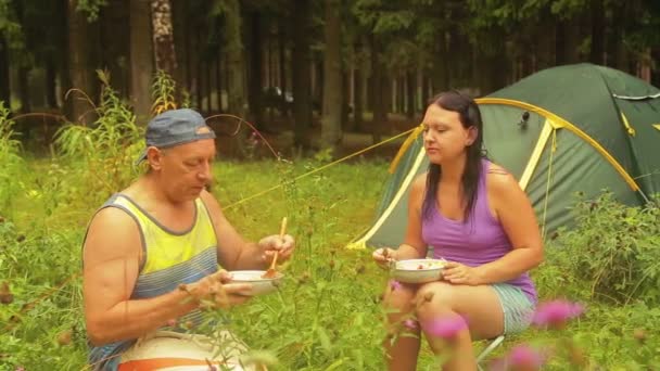 Mann und Frau sitzen in der Nähe eines Zeltes im Wald und essen Obstsalat. — Stockvideo