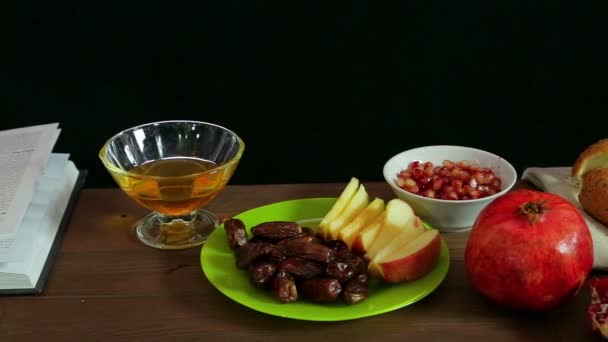 På bordet är traditionella godsaker på Rosh Hashana: granatäpple, äpple, honung och hala. Nästa en festlig bönbok och en menorah med ljus. — Stockvideo