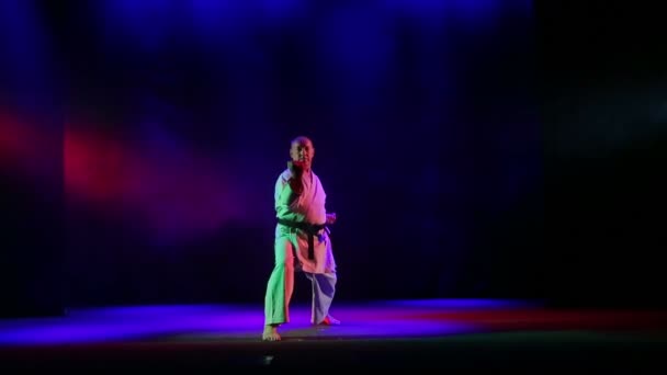 Un uomo in kimano con cintura nera è impegnato nel karate su sfondo nero con fumo colorato — Video Stock