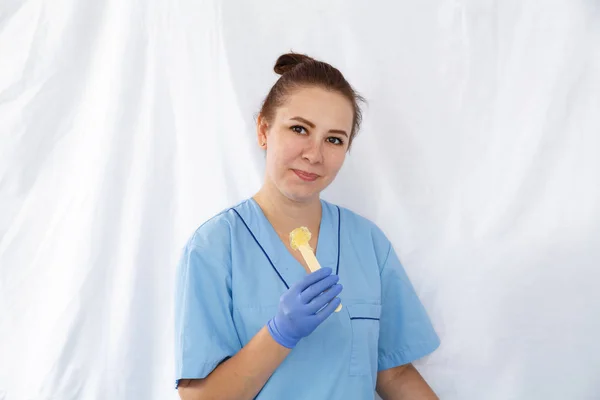 Женщина-косметолог держит лопатку с сахарной пастой в руке — стоковое фото