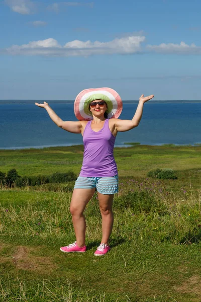 Ung kvinna i en hatt och solglasögon på sjön bakgrund. — Stockfoto