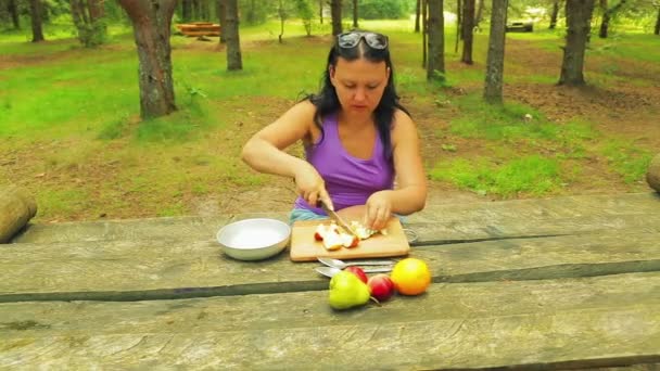 Fiatal nő, egy parkban, egy fából készült asztal szeletelés egy alma, egy salátát, a szeletekre. — Stock videók