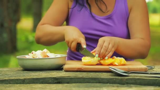 Las manos femeninas cortan una naranja en trozos para una ensalada de frutas . — Vídeo de stock