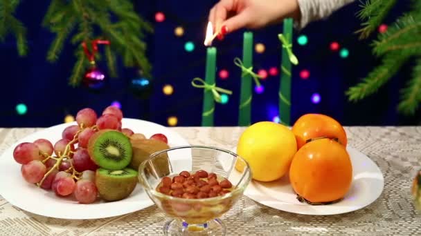 Plody jsou na stole vánoční strom zdobený koule a blikající světla na stranu. V pozadí žena světla svíčky nový rok