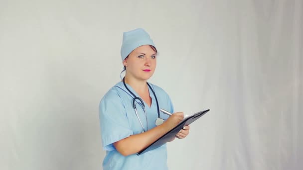 Médico femenino mira hacia otro lado y comienza a escribir la receta pluma — Vídeos de Stock
