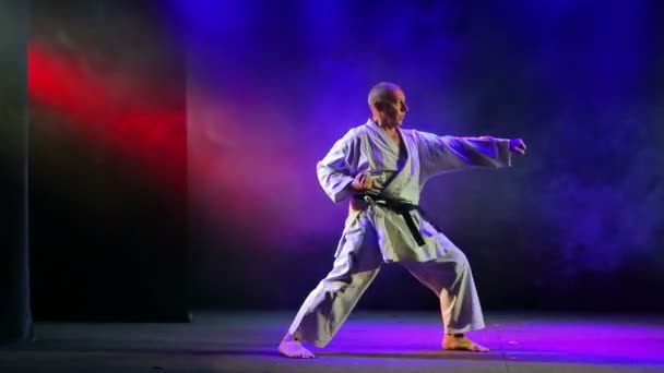 De man toont techniek van karate op een achtergrond met gekleurde rook — Stockvideo