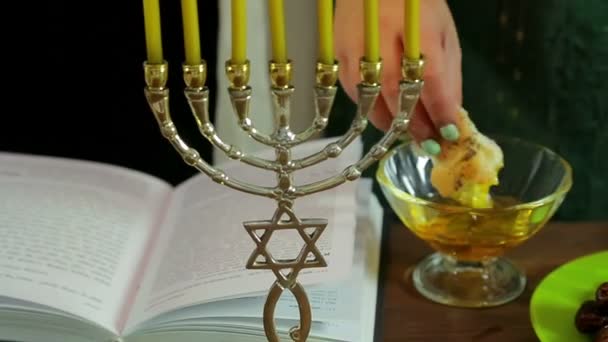 Eine Frauenhand tupft einen Heiligenschein in eine Tasse Honig. im Vordergrund der Menora mit Kerzen. — Stockvideo