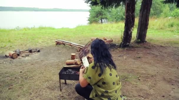 Жінка сидить на барбекю і крутиться над грилем з рибою . — стокове відео