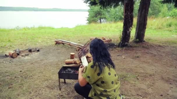 La mujer se sienta en la barbacoa y gira la parrilla con un pescado . — Vídeo de stock