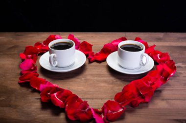 İki bardak kahve ahşap bir masa içinde gül yaprakları gibi bir kalbi vardır. Yatay çerçeve