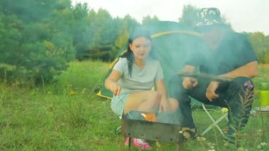 Bir erkek ve bir kadın çadırın oturan ve ızgara et ızgara.