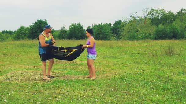 Un uomo e una donna aprirono e stesero una tenda a terra per l'assemblea . — Video Stock