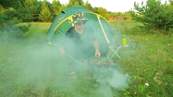 Un homme près de la tente grille la viande sur le gril . — Video