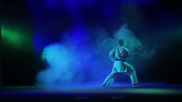 Un maestro de karate con un cinturón negro sobre un fondo negro se dedica al karate — Vídeos de Stock