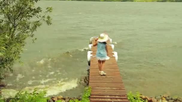 Una mujer joven está de pie en un muelle en la tormenta y mirando las olas . — Vídeos de Stock