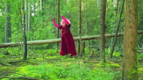 Eine junge Hexe in Rot im Wald tanzt einen rituellen Tanz mit einem Stab. — Stockvideo