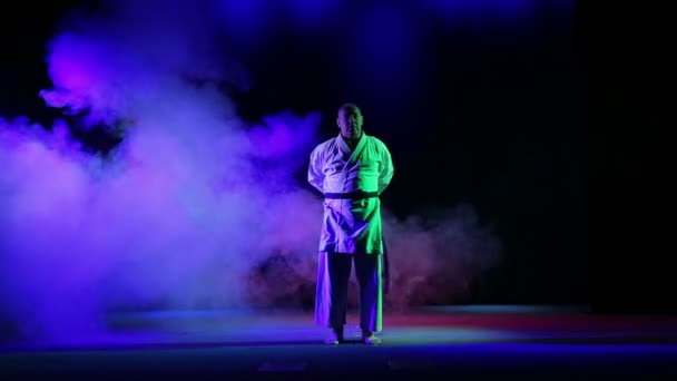 En man binder upp en svart karate bälte mot en bakgrund av färgad rök — Stockvideo