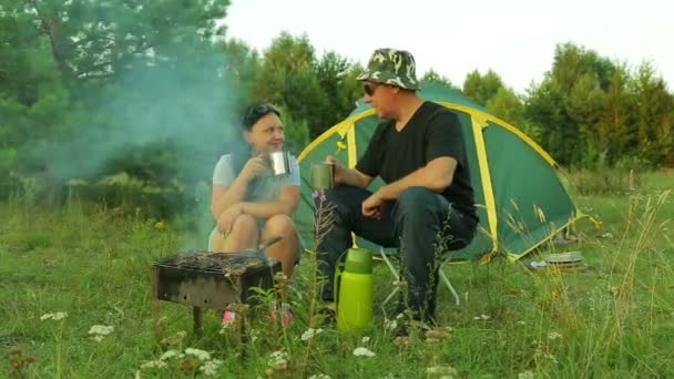 Mężczyzna i kobieta w pobliżu namiotu grillowania mięsa na grilla i picie herbaty. — Wideo stockowe