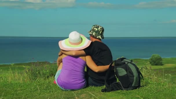 Liefhebbers zitten op de top van de berg en bewonder het uitzicht op het meer. schieten vanaf de achterkant. — Stockvideo