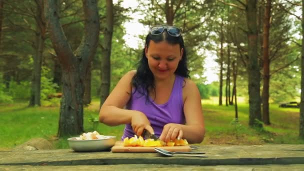 Een vrouw in het park plakjes een sinaasappel in stukjes voor een fruitsalade op een picknick. — Stockvideo