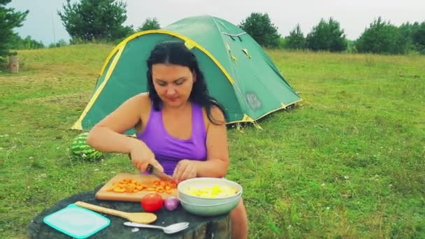 一个妇女在一个帐篷附近的森林空地把胡萝卜切成片, 在一个木桌上的蔬菜躺在. — 图库视频影像