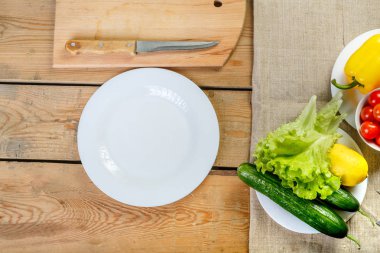 ahşap bir masa üzerinde beyaz bir tabak ve taze sebze olduğunu